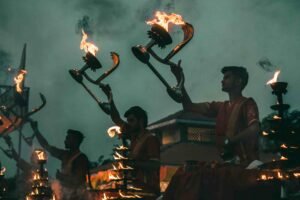 Priests performing evening Ganga Aarti with fire lamps at the riverbank, surrounded by devotees.

